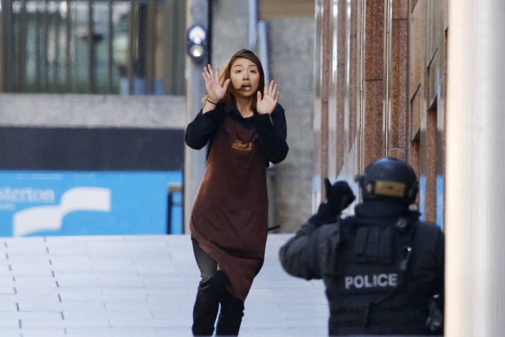 A hostage runs towards a police officer outside Lindt cafe, where other hostages are being held, in central Sydney